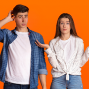 A young man and woman stand against an orange background, both looking confused. As part of the 30 Days Summer Consistency Challenge, the man scratches his head while the woman shrugs, uncertain how to stay on track. Austin Marathon Half Marathon & 5K