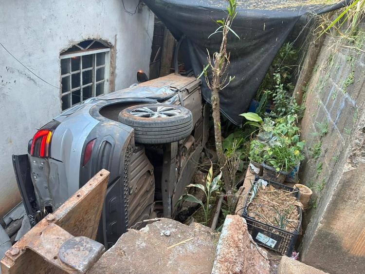 Motorista perde controle de carro, desce barranco e cai entre casas