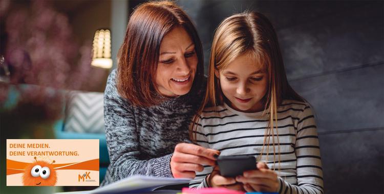 Mutter die mit ihrer Tochter ins Smartphone schaut