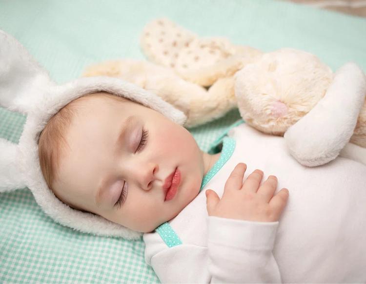 Sleeping baby lying comfortably on a soft mint green blanket with a plush rabbit toy.