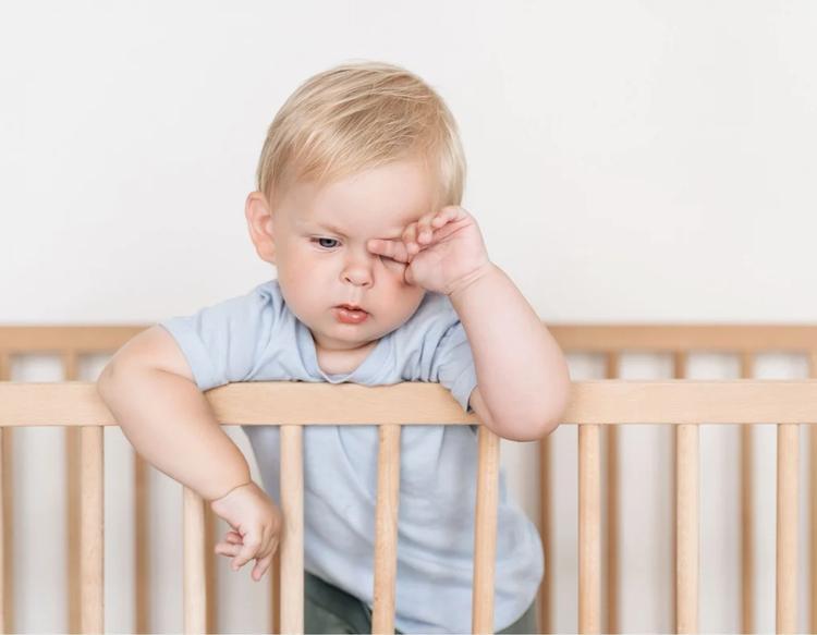Baby boy rubbing itchy eyes in crib during spring seasonal allergy.