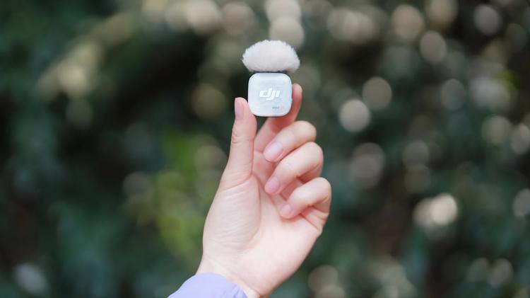 A hand holding up a DJI Mic Mini 2S with a fluffy windscreen attached to it.