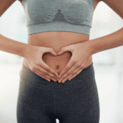 Person in athletic wear forms a heart shape with their hands over their stomach, suggesting health, fitness, or self-care—highlighting the importance of gut training and proper marathon nutrition. Bright, soft background. Austin Marathon Half Marathon & 5K