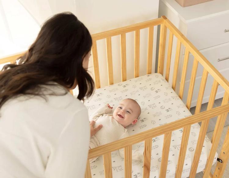 Mother placing her baby into a crib fitted with a soft KeaBabies organic cotton crib sheet.