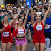 Three runners in red athletic wear from a running crew celebrate with their arms raised while crossing a marathon finish line. Austin Marathon Half Marathon & 5K