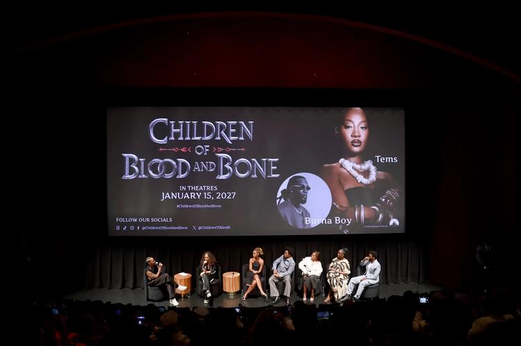 A group of people, including Lena Waithe, Gina Prince-Bythewood, Thuso Mbedu, Tosin Cole, Regina King, Lashana Lynch, and Zackary Momoh, speaking on stage in front of a large movie poster for 