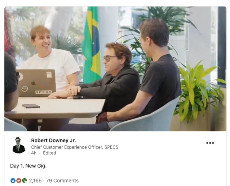 Screenshot of Robert Downey Jr.’s LinkedIn post reading “Day 1. New Gig,” with a video still showing him seated with colleagues at a table. His profile lists his title as Chief Customer Experience Officer at SPECS.