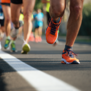Close-up of runners' legs and feet during a race, with one in bright orange shoes leading the way. The image captures energy and motion, inspiring you to increase mileage and build running distance while avoiding burnout. Austin Marathon Half Marathon & 5K