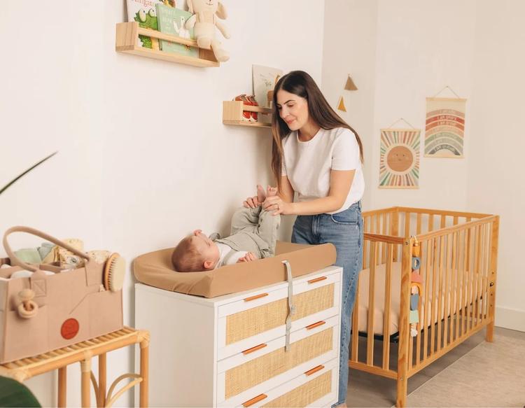 Mom changing baby’s diaper on a changing counter with organized diapering essentials in a nursery setup.