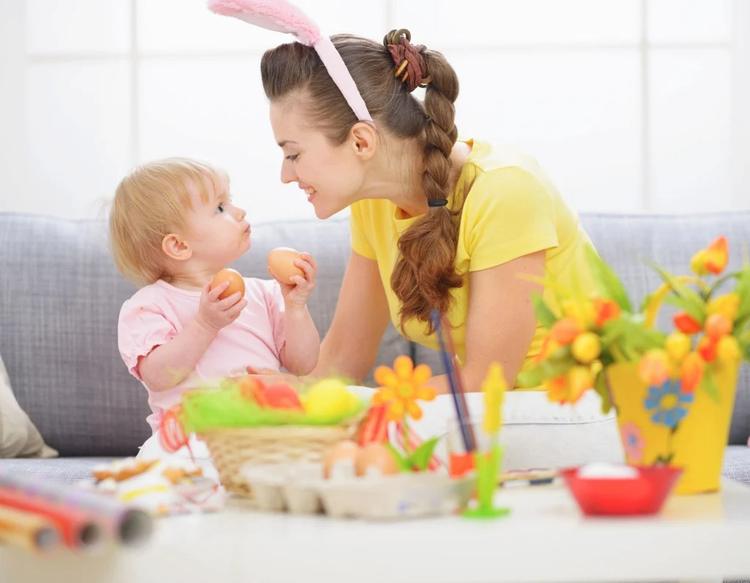A mother smiling at her baby while they reach for Easter eggs.