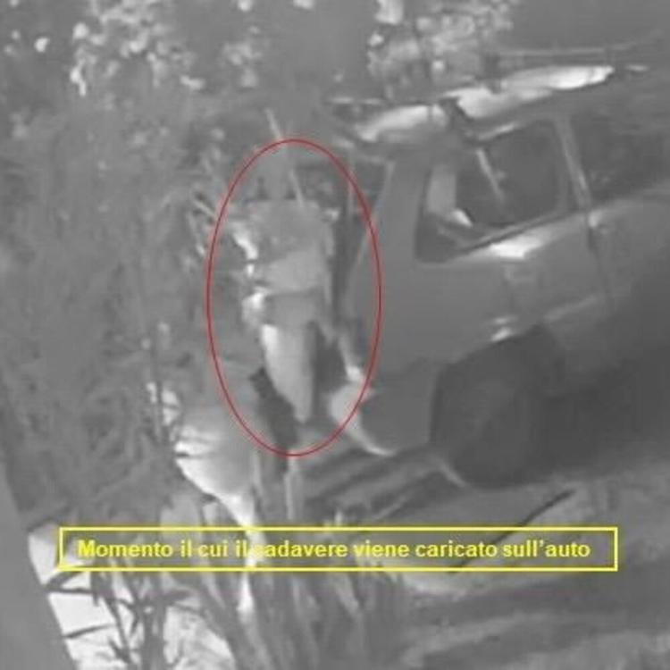 Le telecamere riprendono il momento in cui il cadavere avvolto in un lenzuolo viene carica...