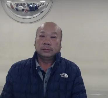 An older Asian man wearing a navy blue jacket and looking directly at the camera.