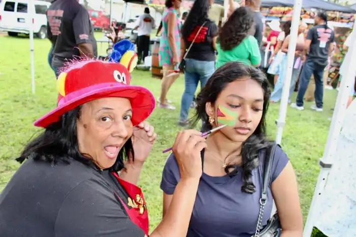 Pandora, the face painter, is excited after completing artwork of Guyana's national flag on the cheek of a heritage fan on August 16, during a crowded-pleasing 9th Queens International Food and Music Festival at Smokey Oval Park in South Richmond Hill.