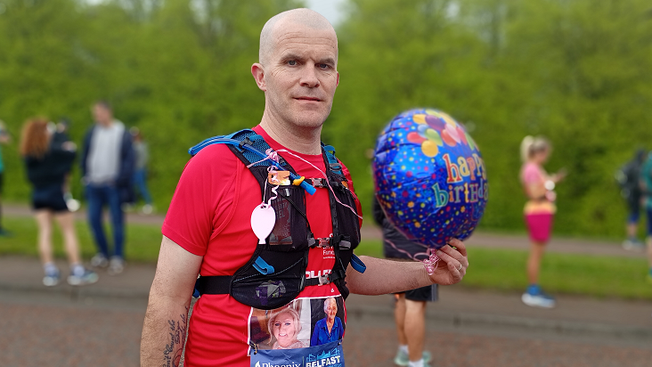 Stephen Perry, a man with a shaved head poses with a helium 