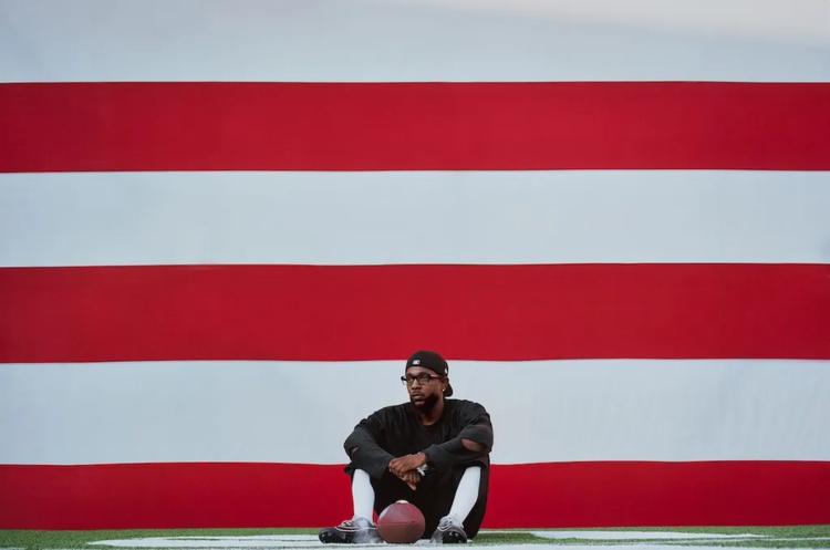 A person sitting on a football field in front of a large red and white striped backdrop with the text 