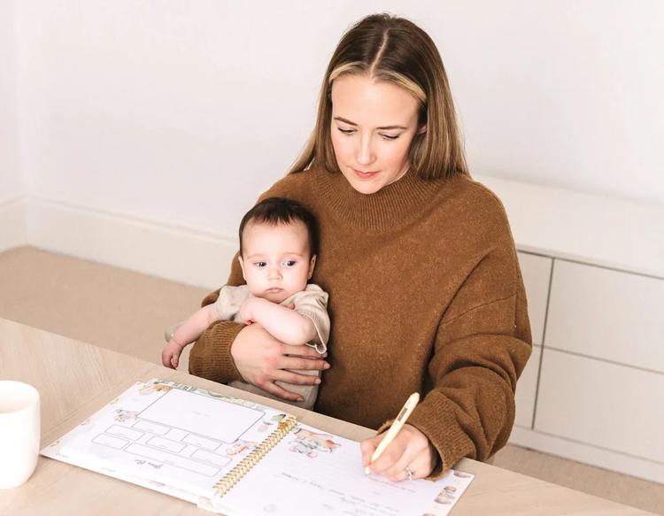 Mom writing in a KeaBabies memory book, recording baby milestones and special details in a keepsake journal.