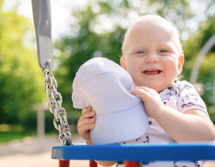 Baby boy playing happily at an outdoor playground during a sunny day.