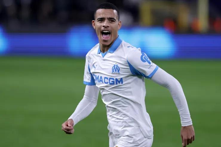 Greenwood esulta durante una partita in maglia bianca e blu, campo da calcio sullo sfondo
