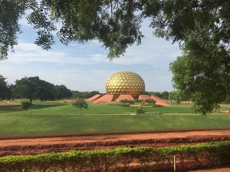 The Matramandir in Auroville, which looks like a golden sphere made of many circular golden tiles, sitting on a red soil based within green manicured lawns