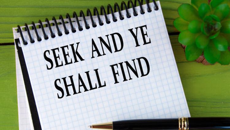 SEEK AND YE SHALL FIND - words in a white notebook on a green wooden background with a cactus and a pen