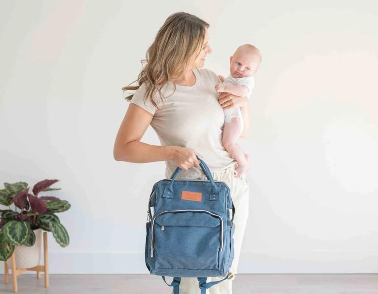 Mother carrying her baby and a diaper bag while getting ready for an outdoor stroll and family outing.