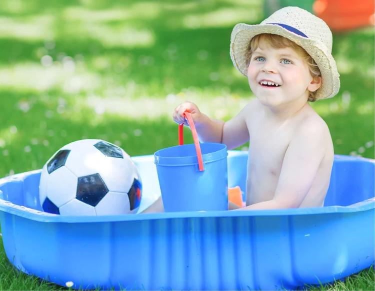 Little toddler boy splashing water in the backyard garden on a sunny summer day, enjoying outdoor water play at home.