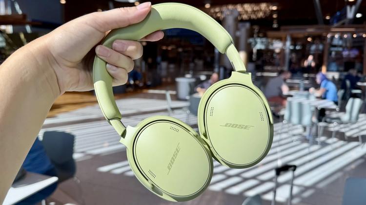 person holding green bose headphones in front of airport terminal