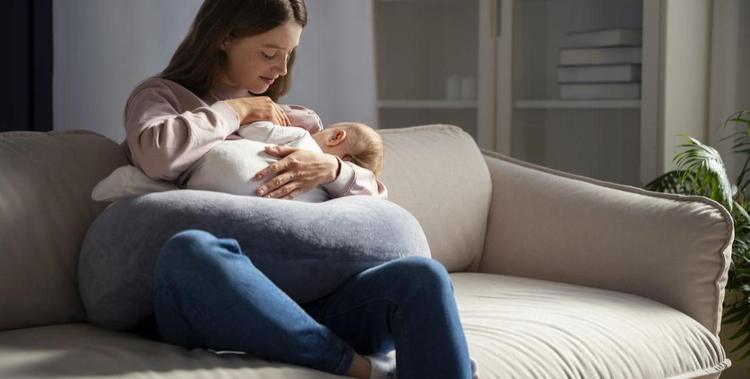  Mutter die auf der Couch sitzt und ihr Säugling stillt