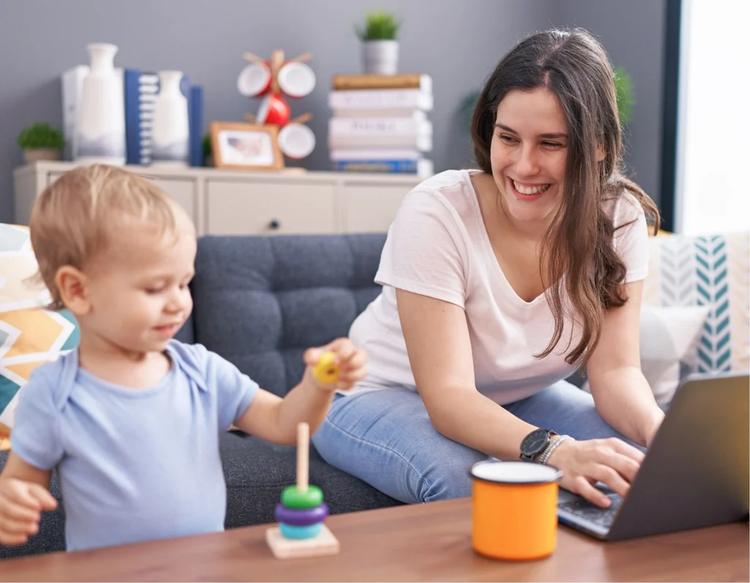 Mother and son using a laptop at home, enjoying playtime together while mom checks tasks online in a relaxed indoor setting.