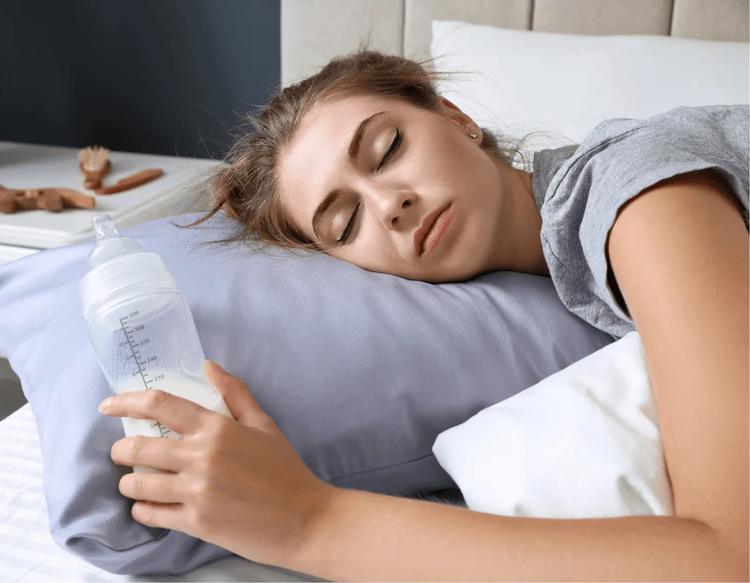 Tired postpartum mom lying in bed holding baby bottle for a quick rest.
