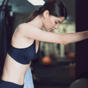 A woman in a black sports bra rests at the gym with a towel, focusing on her exercise recovery. Austin Marathon Half Marathon & 5K