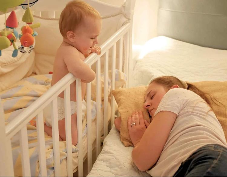 Baby standing in a crib during the middle of the night while crying and throwing a tantrum, highlighting nighttime wake-ups, infant sleep regression, and common baby sleep challenges for parents.