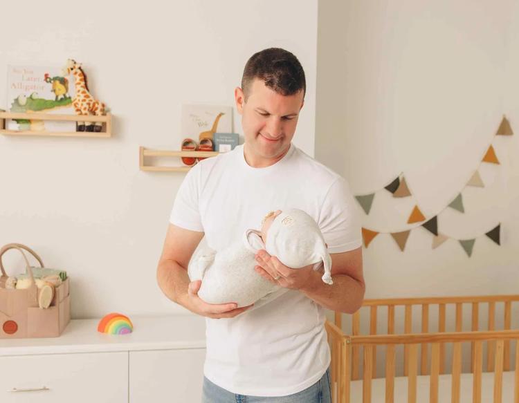 Dad carrying baby wrapped in a KeaBabies Soothe Swaddle Wrap with a Knot Hat.