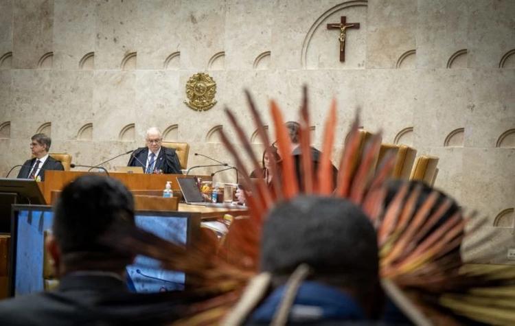 Foto colorida de sessão do Supremo Tribunal Federal, em que aparece um indígena de cocar de costas e, ao fundo, magistrados