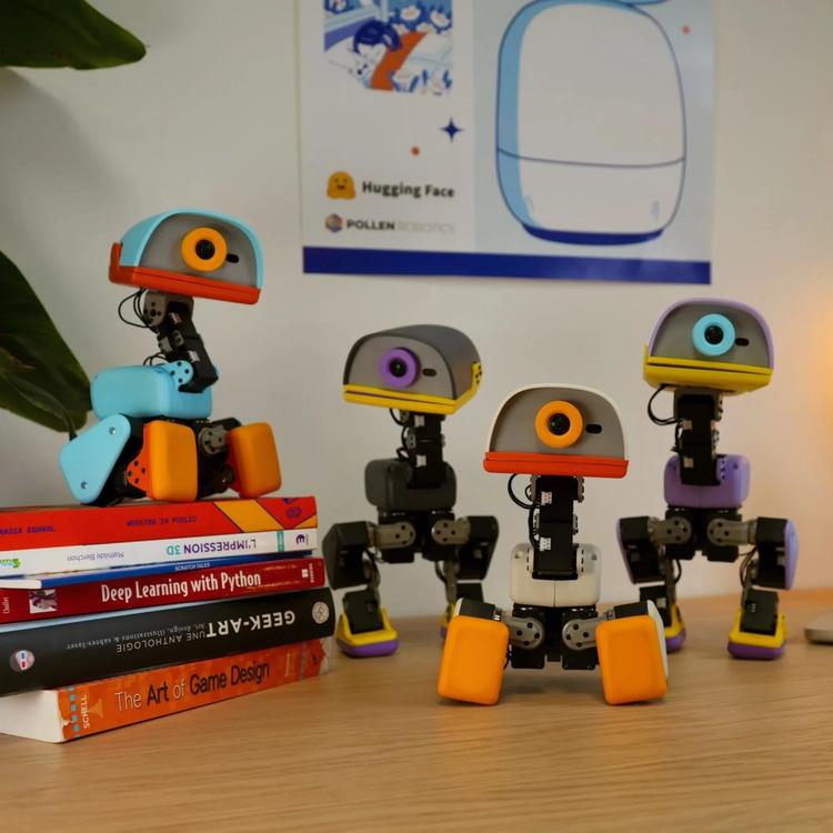 Four colorful Microduck humanoid robots sit together on a desk beside a stack of books.