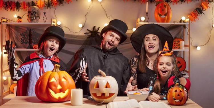  Familie sitzt zu Halloween verkleidet am Tisch mit geschnitzten Kürbissen und Halloween-Dekoration