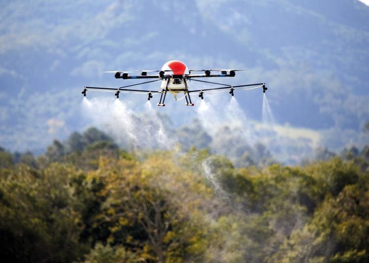 Foto colorida de drone pelicano lançando agrotóxicos. O drone está no alto e abaixo dele aparecem jatos com líquido caindo. Emergência química no Maranhão