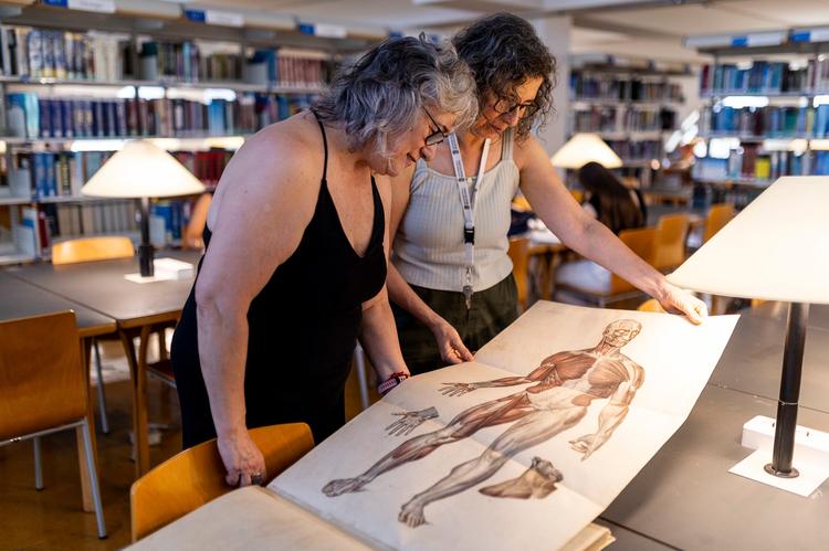 Rosa Zaborras (izq.) y Marta Mercader, bibliotecarias en la Facultad de Medicina de la Universidad de Barcelona consultan el libro 'Anatomie élémentaire', publicado el año 1843, donde predominan modelos masculinos para ilustrar el cuerpo humano. 
