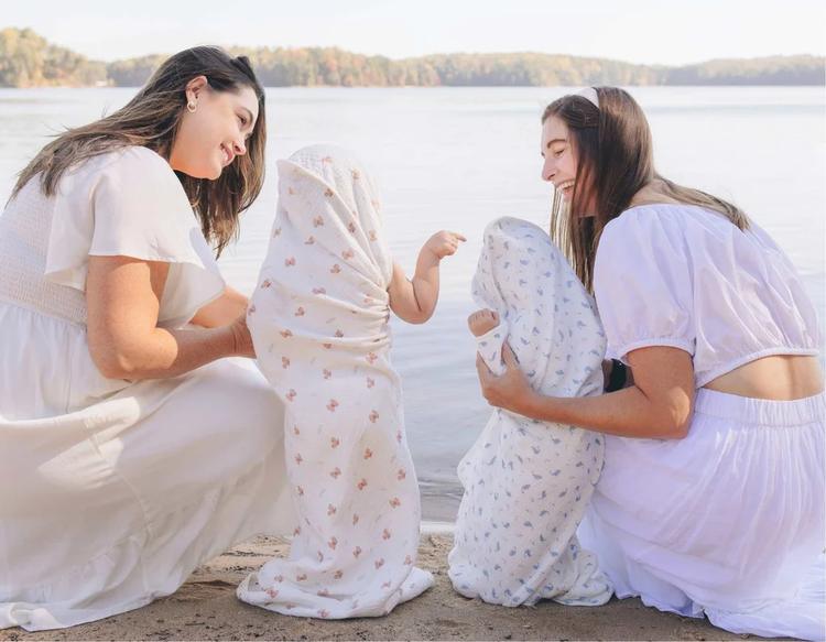 Mom bonding with her child wrapped in a KeaBabies Lyra Muslin Hooded Towel by the lakeside after water play, enjoying a fun summer day outdoors.