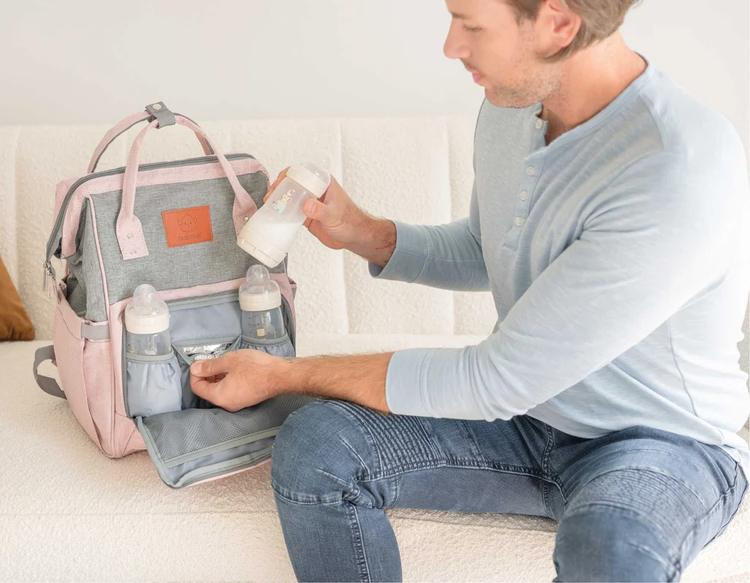 A dad organizing milk bottles and baby essentials in the KeaBabies Original Diaper Bag before a family road trip.