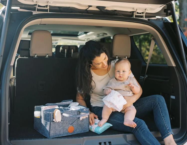 KeaBabies diaper caddy organizer filled with wipes and diapers next to a mom and baby in a vehicle.