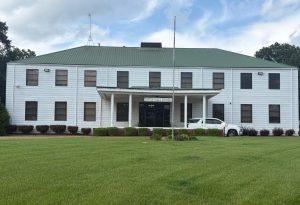 A rectangular white building with a trapezoidal green roof. Seventeen upright rectangular windows cover the front of the building. A lower section marks the entrance and features a white sign reading “Canton Public Schools.”