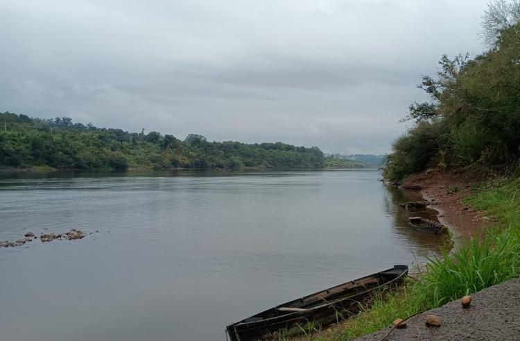 Foto colorida do Rio Taquari, em Arroio do Meio. Na imagem, está nublado e aparece uma canoa próxima da margem do Rio