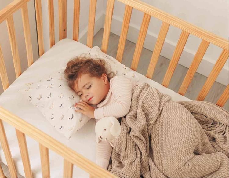 A toddler sleeping peacefully in a crib with the KeaBabies Toddler Pillow.