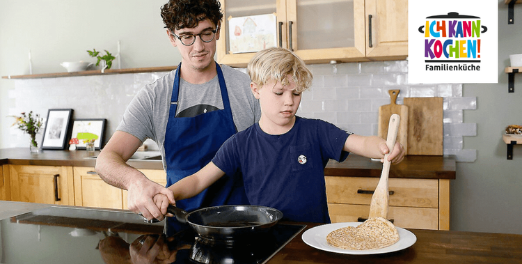 Erwachsener mit Kind am Herd beim Pfannkuchen braten