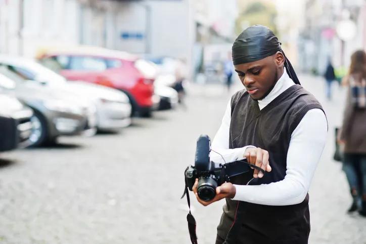 Young professional african american videographer holding professional camera with pro equipment. Afro cameraman wearing black duraq making a videos.