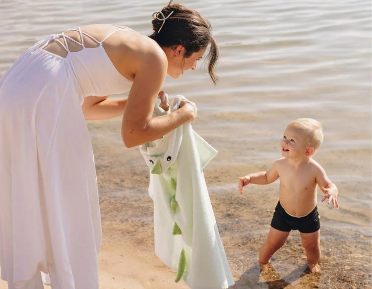 A smiling mother and her toddler enjoying a screen-free day of play by the lake, with the mom carrying a soft PlayPals Hooded Towel for a cozy post-swim dry-off.