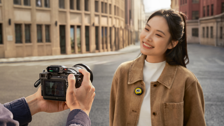 A woman wearing the Insta360 Mic Pro, smiling at a camera with the reciever plugged in.