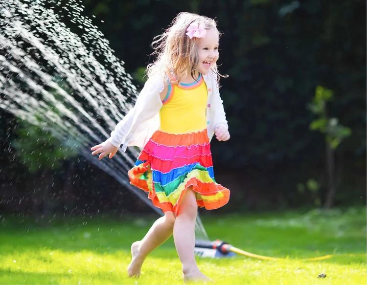 Toddler girl running through a backyard sprinkler on a sunny summer day, enjoying outdoor water play and summertime fun.