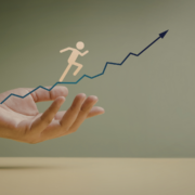 A hand supports a zigzag upward arrow graph with a stick figure running along it, symbolizing Fitness progress and growth—perfect inspiration for your Mid-Year Fitness Check against a neutral background. Austin Marathon Half Marathon & 5K